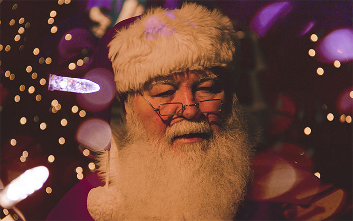 Santa Claus with glasses, surrounded by holiday lights, in a festive setting.