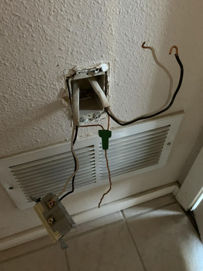 Exposed electrical wires and a loose outlet highlight a cheap construction fail in a wall installation.