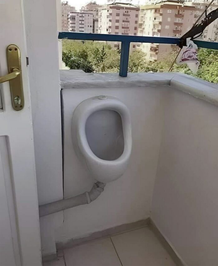 Urinal awkwardly installed on a balcony, showcasing a funny construction fail with a city view in the background.