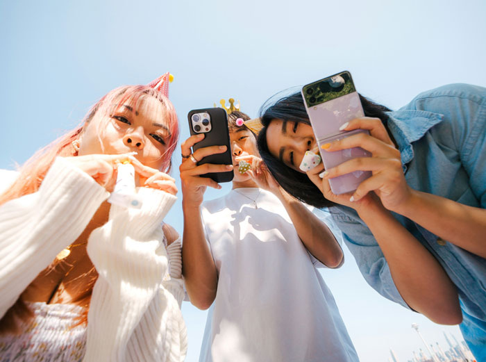 Generation A teens at a party looking at smartphones, wearing festive hats.