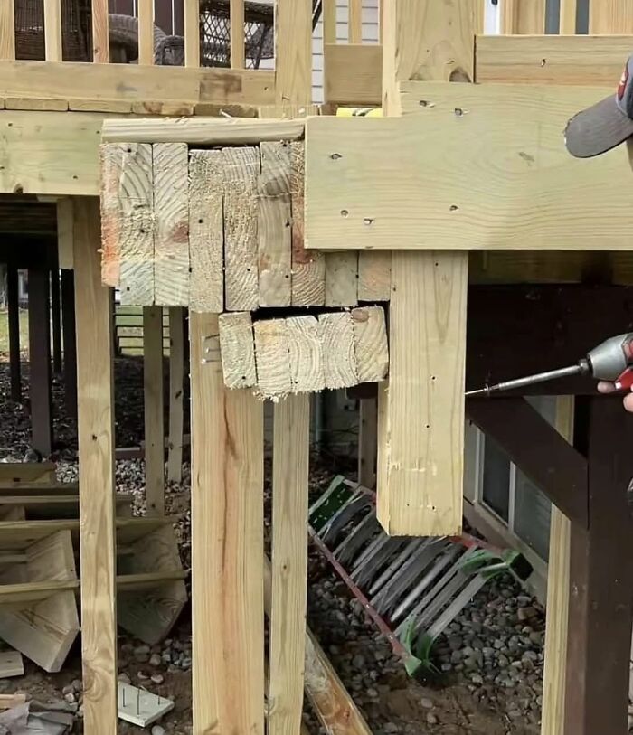 Unstable wooden deck corner showing funny construction fails with layers of misaligned beams.