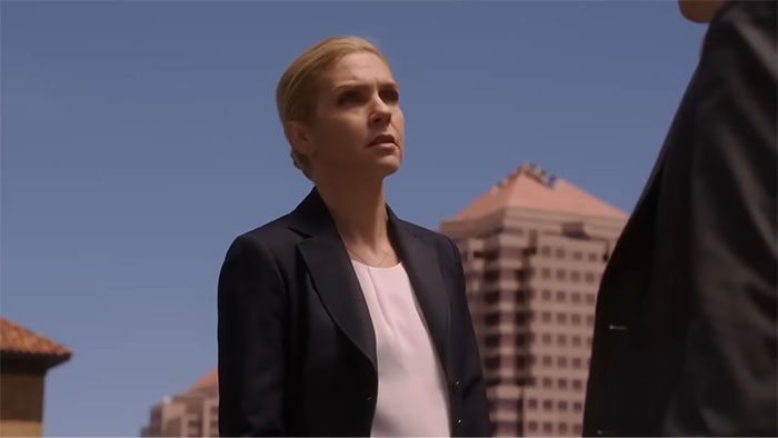 A woman in a business suit stands confidently outside in an urban setting, embodying a strong female protagonist.