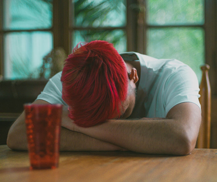 Person with red hair resting head on arms at a table, capturing Gen A's digital fatigue.