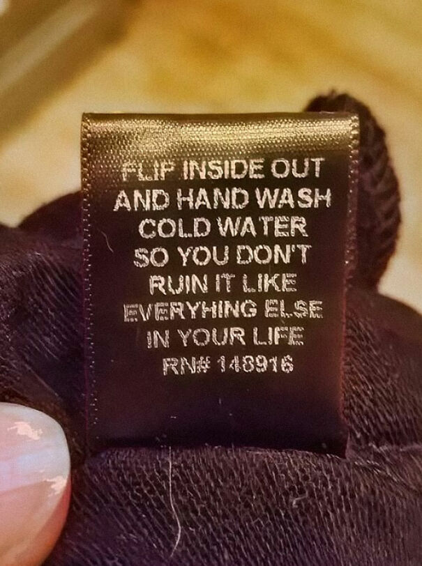 Weird sign on clothing tag with humorous washing instructions for cold water and life advice.