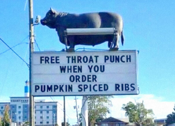 A weird and absurd sign offering a "free throat punch" with pumpkin spiced ribs, with a cow statue on top.