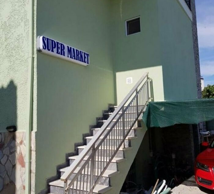 Staircase leading to a wall under a supermarket sign; a construction fail.