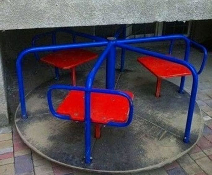 Construction fail with a playground merry-go-round built under a low concrete overhang, making it unusable.