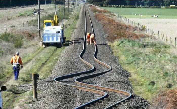 Construction workers inspecting hilariously bent railroad tracks.