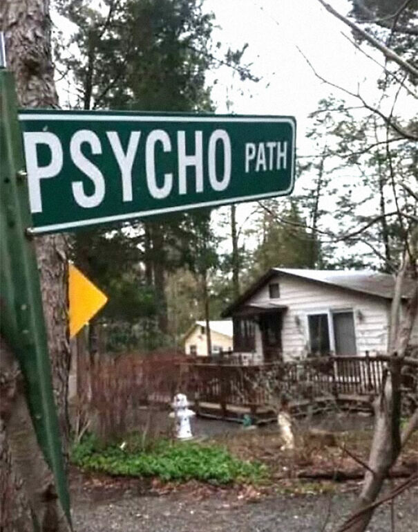 Weird and absurd sign reading "Psycho Path" in front of a small house surrounded by trees.