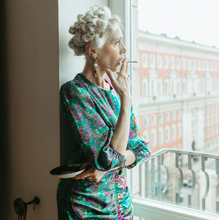 Woman in colorful dress smoking near the window, highlighting third-hand smoke risks.