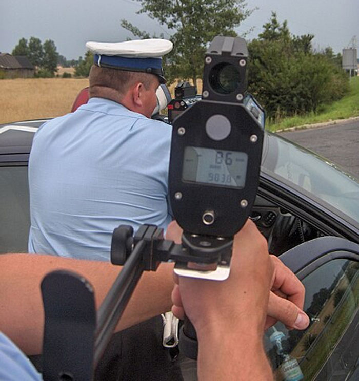 Officer using radar gun to check speed on a rural road, capturing genuine speeding reasons from drivers.