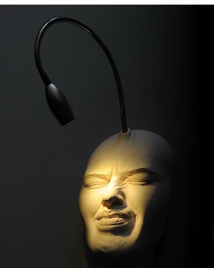 Realism and surrealism merge in expressive sculpture of a face illuminated by a lamp.