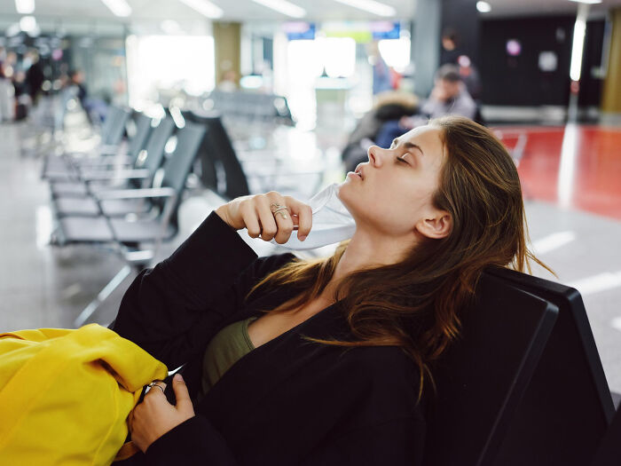 Woman looking stressed in an airport, holding a face mask.