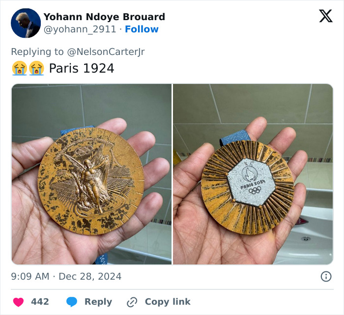 Hand holding rusted bronze medals from Paris 2024 Olympics in a bathroom setting.