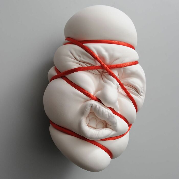 Surreal sculpture blending realism with red rope details, showcasing expressive facial features.