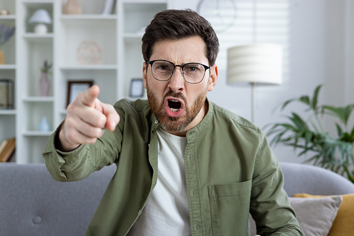 Man expressing anger, pointing finger, possibly during a lying test scenario in a modern living room setting.