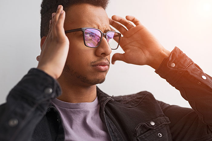 A man with glasses and a thoughtful expression, adjusting his black jacket.