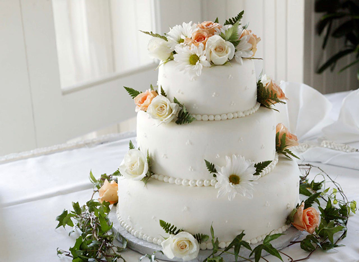 Three-tier wedding cake with floral decoration on a white tablecloth.