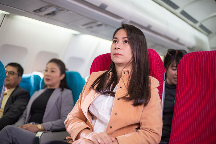 Passenger on a plane looks upset, sitting upright in her red seat, surrounded by other travelers, related to seat denial incident.