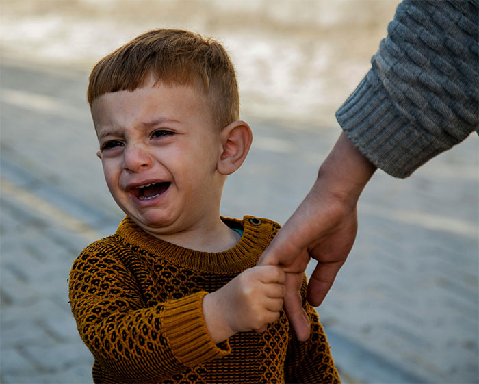 A crying child in a brown sweater holds a parent's hand, symbolizing a temperamental moment.