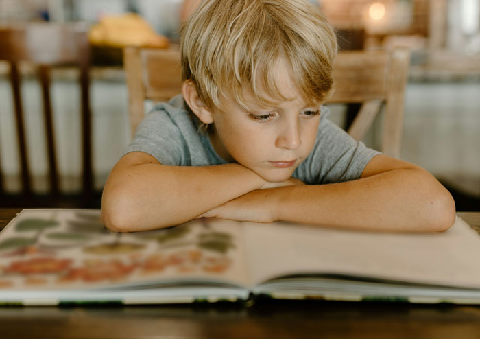 Child from Gen A engrossed in reading a book at a wooden table, highlighting non-digital learning habits.