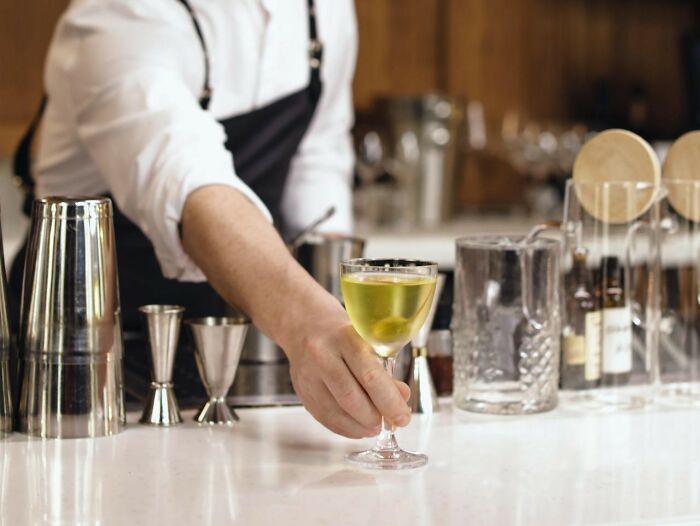 Bartender serving a cocktail with an outstretched hand, showcasing a scene from workplace scenarios involving quick job changes.