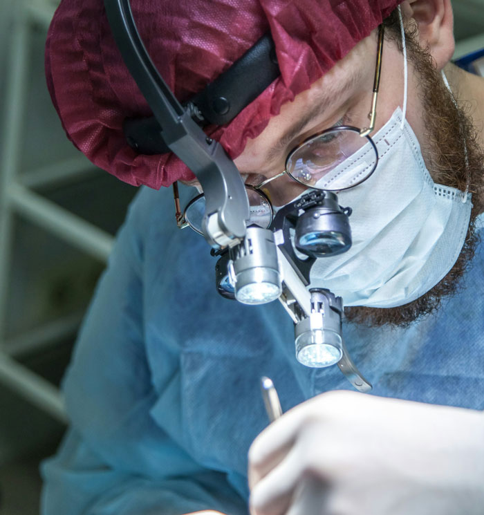 A focused surgeon in a mask and magnifying glasses performing a procedure.