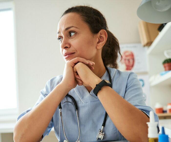 A medical professional in blue scrubs, deep in thought, illustrating the reality behind 'fun' jobs.