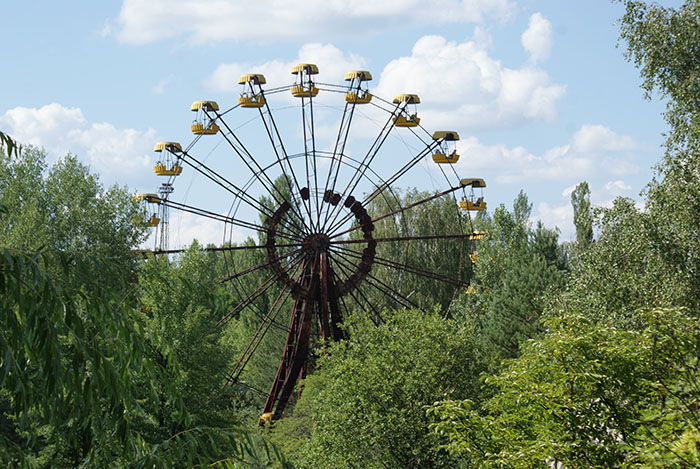 Ferris wheel in Chornobyl area surrounded by dense greenery on a sunny day.