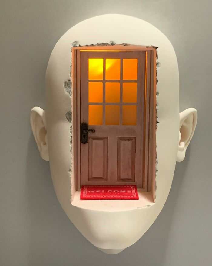 Surrealist sculpture of a human face with a door and welcome mat, blending realism and surrealism in art.