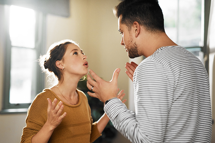 A dad babysits, appearing frustrated, while having a discussion with a woman in a cozy room setting.