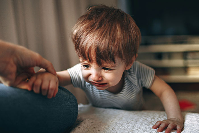 A toddler crying indoors, reaching for a person’s hand, possibly related to a concussion.