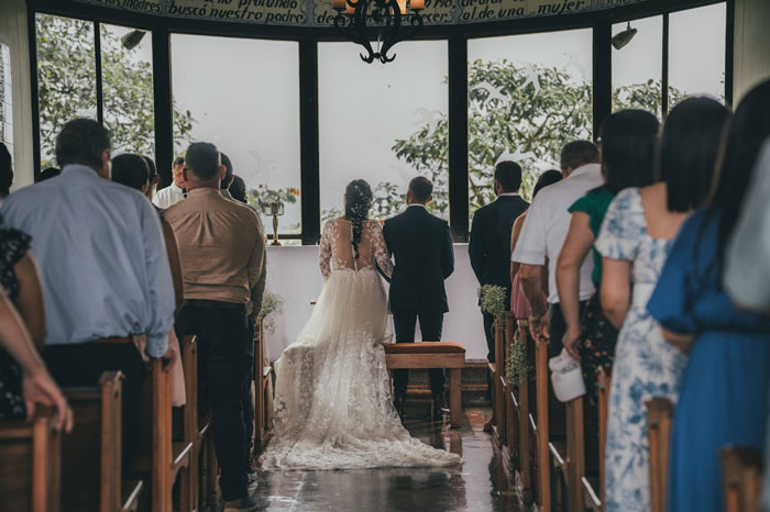 Wedding ceremony in a church, bride in a lace gown and groom at the altar, surrounded by guests.