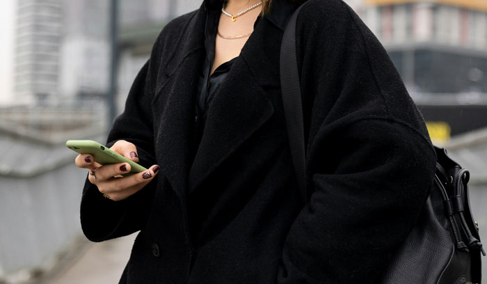 Person in black coat using a smartphone, representing Gen A technology interaction.