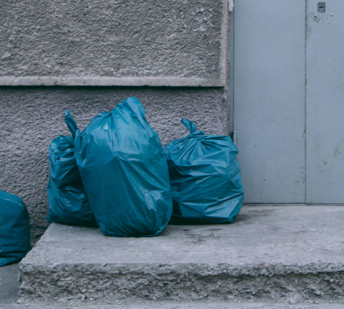 Four blue trash bags on the sidewalk near a gray wall, symbolizing reasons for being fired.