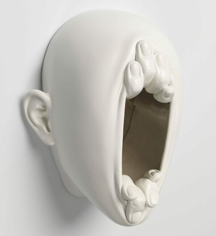 Surrealist sculpture blending realism with expressive hands emerging from a blank face.