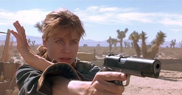 A strong female protagonist aiming a handgun, set in a desert environment.