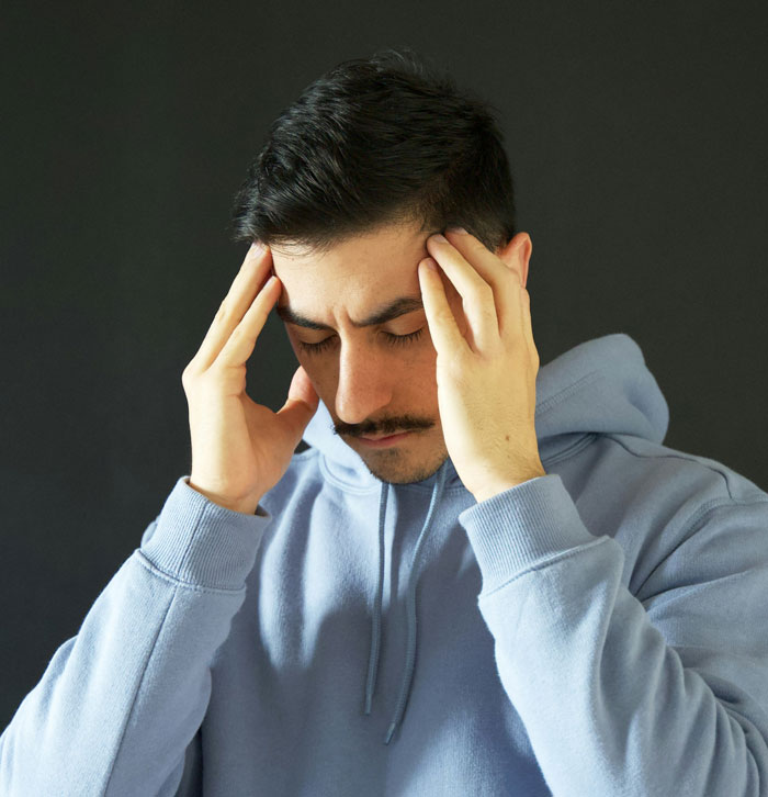 A person in a blue hoodie looking stressed, holding their head.