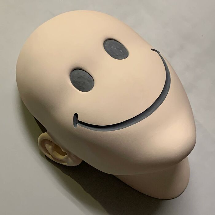 Surreal sculptural artwork blending realism with a large head and a smiley face design.