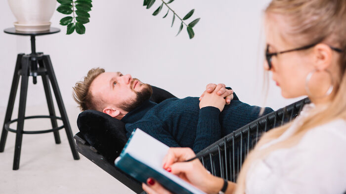 Man lying on a couch, talking to a woman with a notebook, embodying the "HR not your friend" narrative.