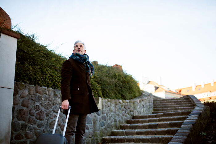 Man with suitcase gazing up stone steps, representing aging challenges.