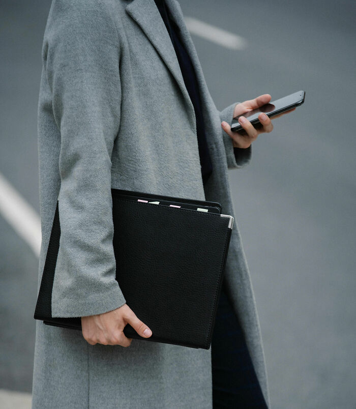 Person in a gray coat holding a phone and clipboard, representing security measures awareness.