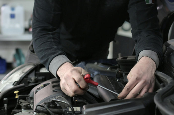 Mechanic working on a car engine, using a tool, in a garage setting.