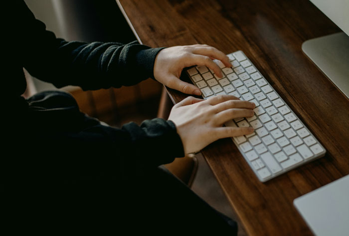 Person typing on a keyboard at a wooden desk, related to reasons for being fired.