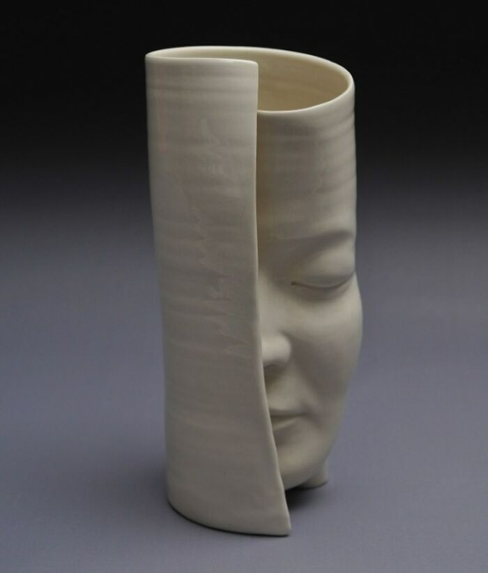 Ceramic sculpture blending realism and surrealism, featuring a partially concealed human face in a cylindrical form.