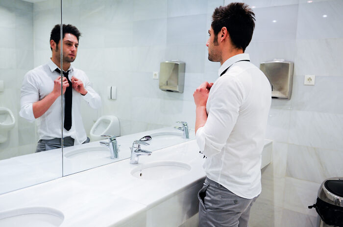 Man in a bathroom adjusting tie, reflecting on HR is not your friend in a corporate setting.