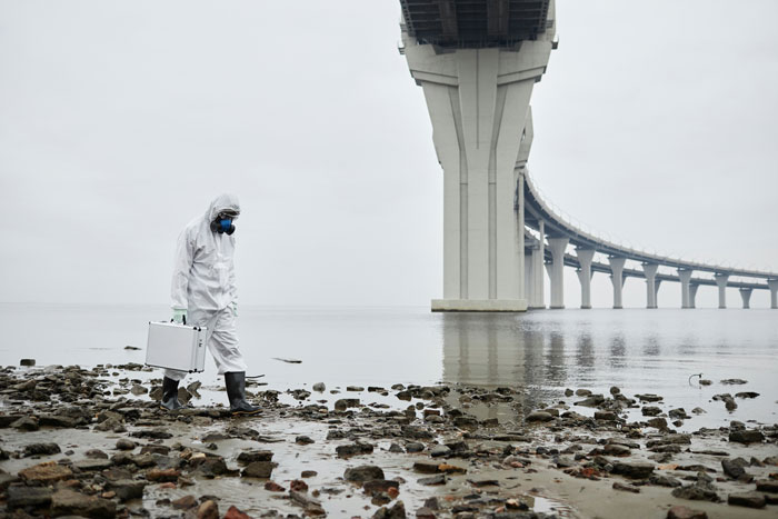 Person in protective gear walks by a bridge, holding a case, highlighting technology gaps in Gen A.