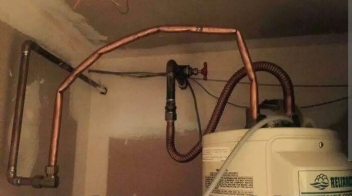 Amateur plumbing job with bent copper pipes, showcasing cheap construction fails in a water heater installation.