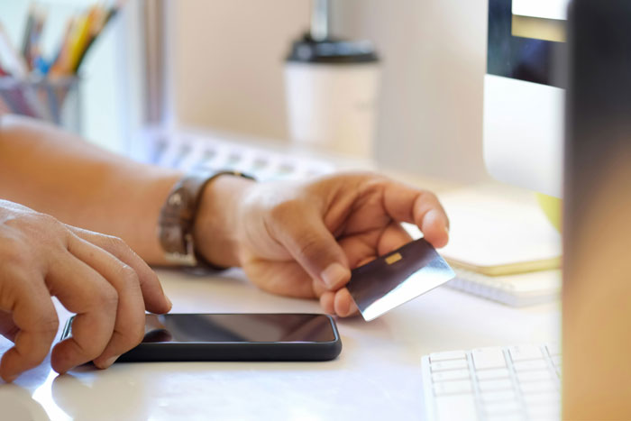 Person holding a credit card and smartphone, focusing on online security measures at a computer desk.