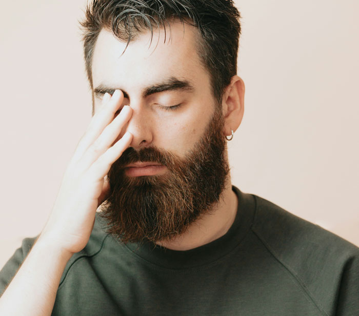 Man with a beard and hand on face wearing an earring, looking stressed about getting fired.